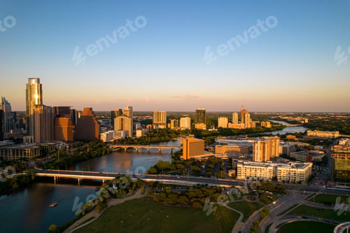Preview: Drone shot of TX skyline with waterfront, greenery and blue sky at sunset in Austin city