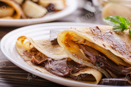 Preview: French crepes with chocolate sauce and banana in ceramic dish on