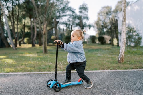 Preview: Little girl rides a scooter across an asphalt yard pushing off with her foot