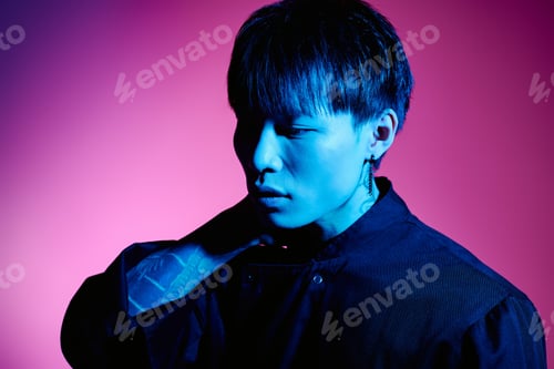 Preview: Stylish young Asian man poses against a vibrant pink and blue studio backdrop