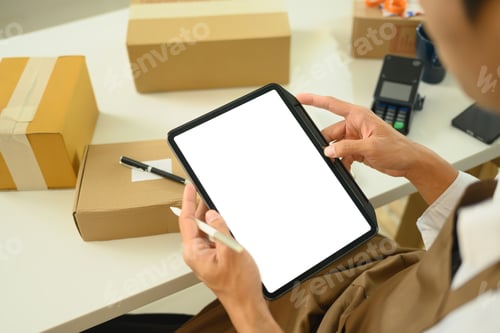 Preview: Small business owner managing orders on digital tablet and preparing packages for shipment