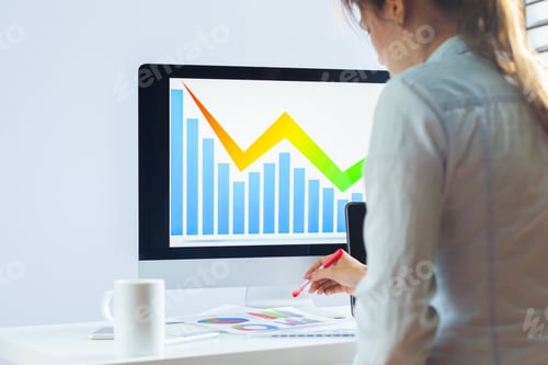 Preview: Business person observes data trends on computer screen while taking notes in office