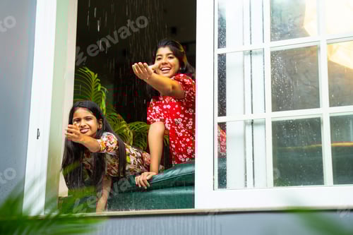 Preview: Two Indian girls happily enjoy monsoon rain while touching water drops from open home window