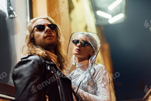 Preview: young attractive couple in stylish clothes looking away on street at night