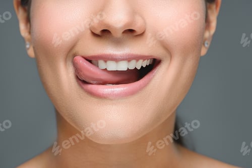 Preview: partial view of smiling woman with white teeth sticking tongue out isolated on grey