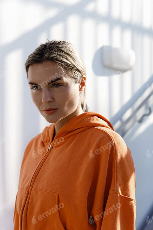 Preview: Young Woman Fitness Enthusiast Wearing an Orange Hoodie Resting Outdoors