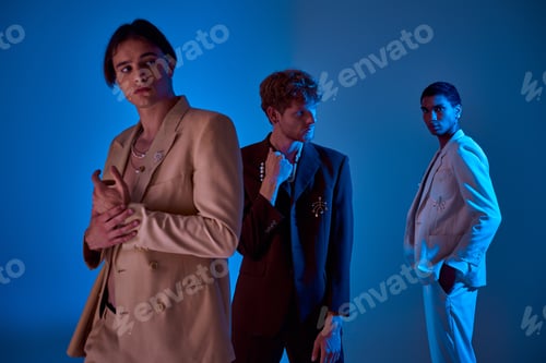 Preview: three young elegant men posing on blue backdrop in classy suits, blue lights, fashion concept