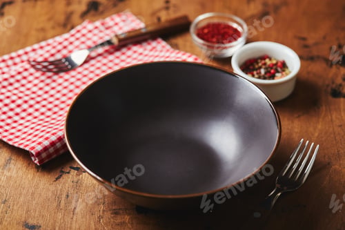 Preview: Empty dark bowl with fork, napkin and spices on wooden background