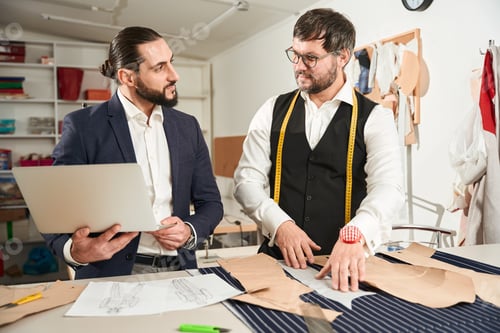 Preview: Tailors Discussing Designs in Workshop Using Laptop