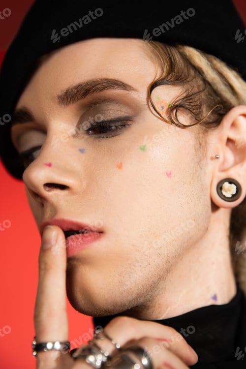 Preview: close up portrait of tattooed queer person with makeup touching lips isolated on orange