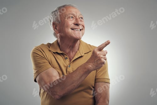 Preview: Studio shot of an elderly man pointing in at something and smiling against a grey background