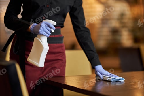 Preview: Schooled waitress sanitizing table surface regularly with special spray