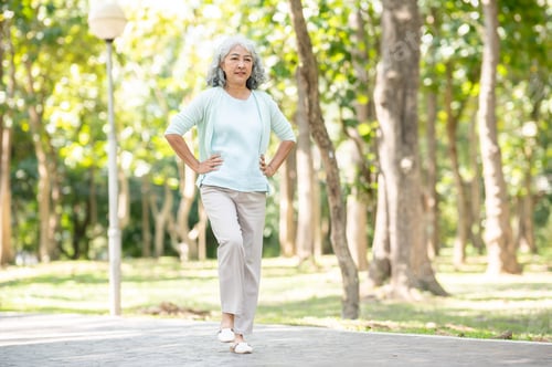Preview: Old age asian woman grandmother put hands on waist lifting a leg while walking or exercising in park