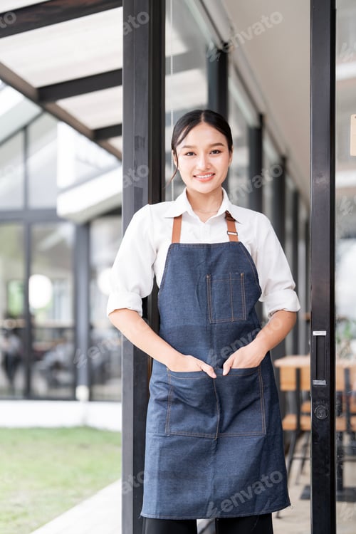 Preview: Small business owner at entrance looking at camera, young female waitress standing at her shop.