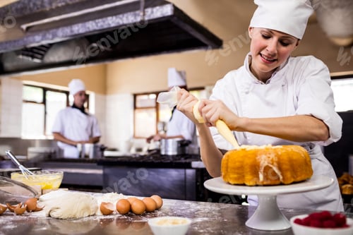Preview: Female chef piping a cake in kitchen at hotel