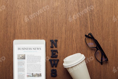 Preview: top view of digital tablet with business news on screen near news lettering, glasses and paper cup