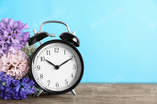 Preview: Black alarm clock and spring flowers on light blue background, space for text. Time change