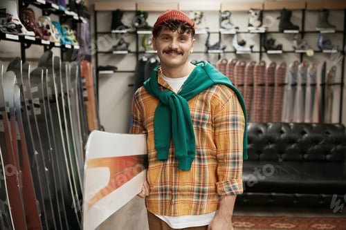 Preview: Portrait of man carrying snowboards equipment over sports shop background