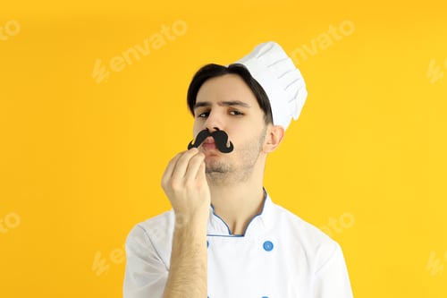 Preview: Concept of cooking, young male chef on yellow background