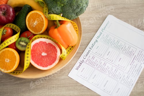 Preview: Weekly eating meal planner and plate of fresh fruits and vegetables nearby on table