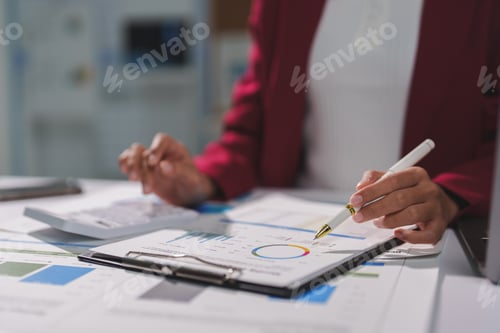 Preview: Businesswoman analyzing financial charts and using calculator in office