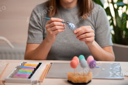 Preview: A beautiful girl paints Easter eggs in the living room. The teenager puts dots on the eggs.