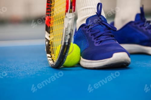 Preview: Legs of young girl in a closed tennis court with ball and racket