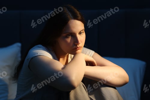 Preview: Sad young woman sitting on bed at home