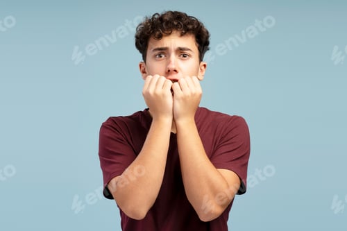Preview: Scared shocked boy, pupil wearing red t shirt looking at camera standing isolated on blue background