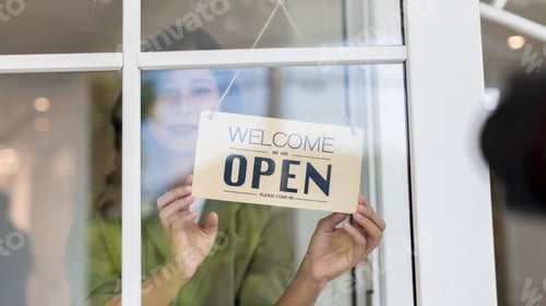Preview: Woman store owner turning open sign broad through the door glass and ready to service. Small busines