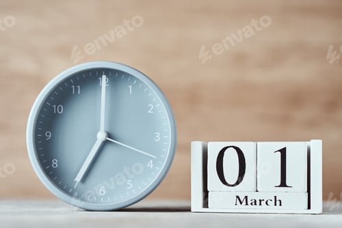 Preview: Alarm clock and wooden block calendar with date 1st march on the table