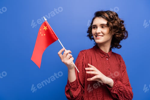 Preview: happy language teacher smiling while holding flag of China isolated on blue