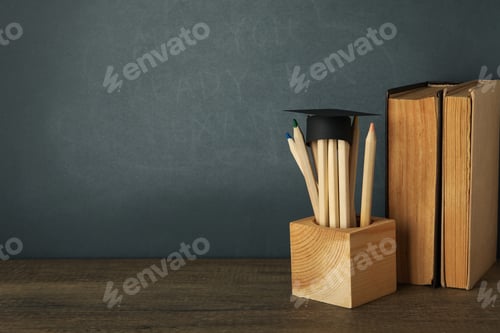 Preview: Graduation hat with books on a table on a dark background.