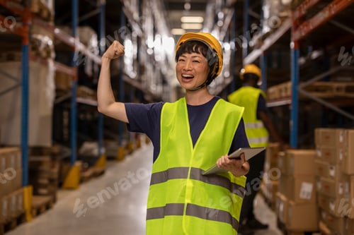 Preview: Asian female worker showing her biceps and holding tablet in warehouse