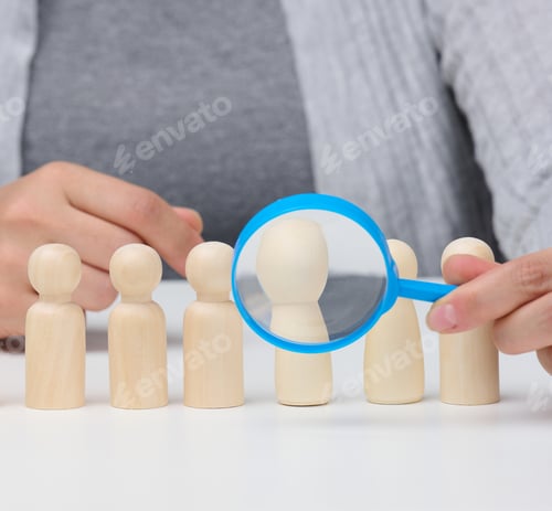 Preview: Figurines of men on a white table, a female hand holds a magnifying glass