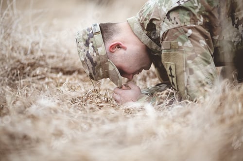 Preview: Shallow focus shot of an American soldier kneeling and praying on a dry grass field