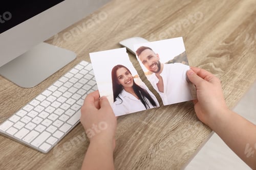 Preview: Woman holding torn photo at wooden table indoors, closeup. Divorce concept