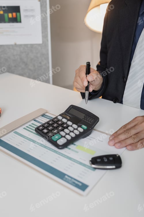 Preview: A businessman in a suit is calculating car loan options using a calculator and comparison chart