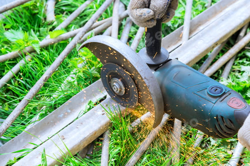 Preview: Worker uses an angle grinder hand saw to a cut metal frames