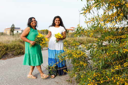 Vista previa: Madre e hija sonriendo sosteniendo flores amarillas al aire libre