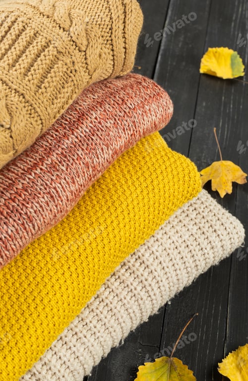 Preview: Warm Knitwear Stacked with Fall Leaves on Dark Surface