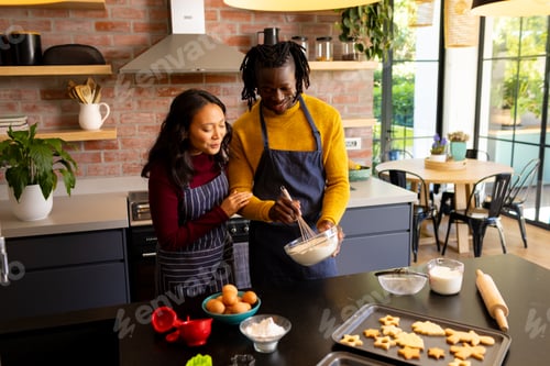 Preview: Happy diverse couple baking christmas cookies mixing dough in sunny kitchen, copy space