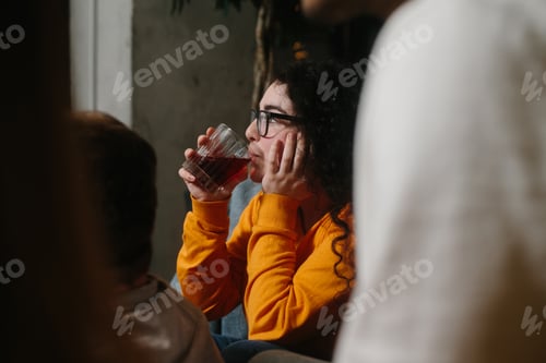 Preview: A young brunette girl in glasses drinks a cocktail and watches a movie in the company of friends.