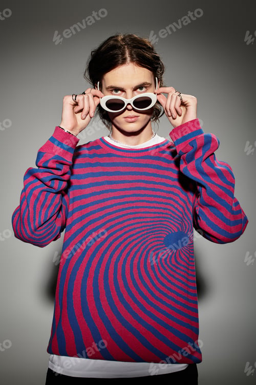 Preview: A stylish young man confidently adjusts his sunglasses while wearing a vibrant sweater.