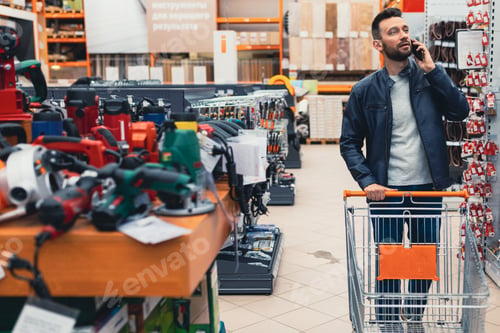 Preview: a buyer in a hardware store walks between the rows with a power tool.