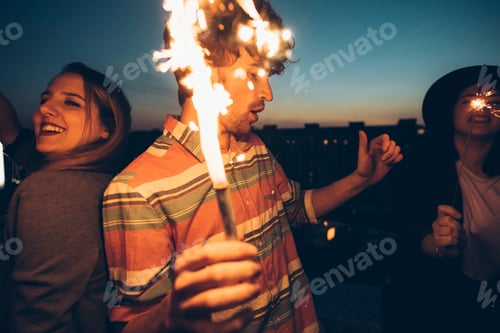Preview: Group of friends enjoying roof party, holding lit sparklers