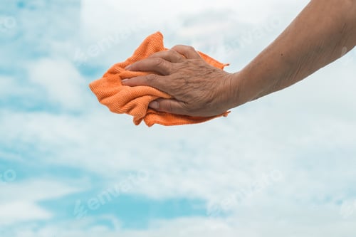 Preview: Home cleaning concept. Senior woman housewife hand using rag and wiping window glass, blurred