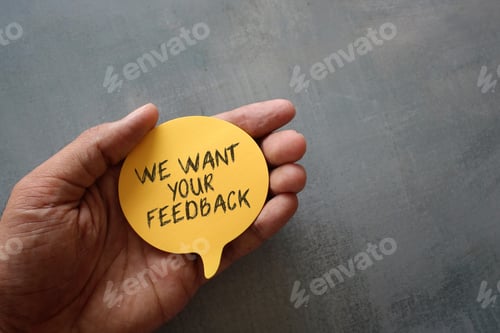 Preview: Hand holding yellow speech bubble with text WE WANT YOUR FEEDBACK with copy space.