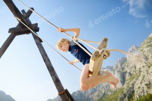 Preview: Little boy having fun on large swing on the shore in the Boka Kotor Bay of the Adriatic Sea