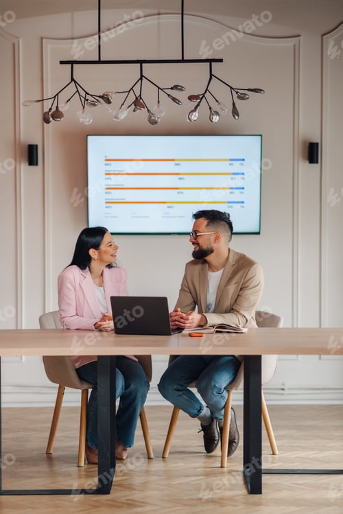 Preview: Business people discussing using laptop in meeting room with charts on screen